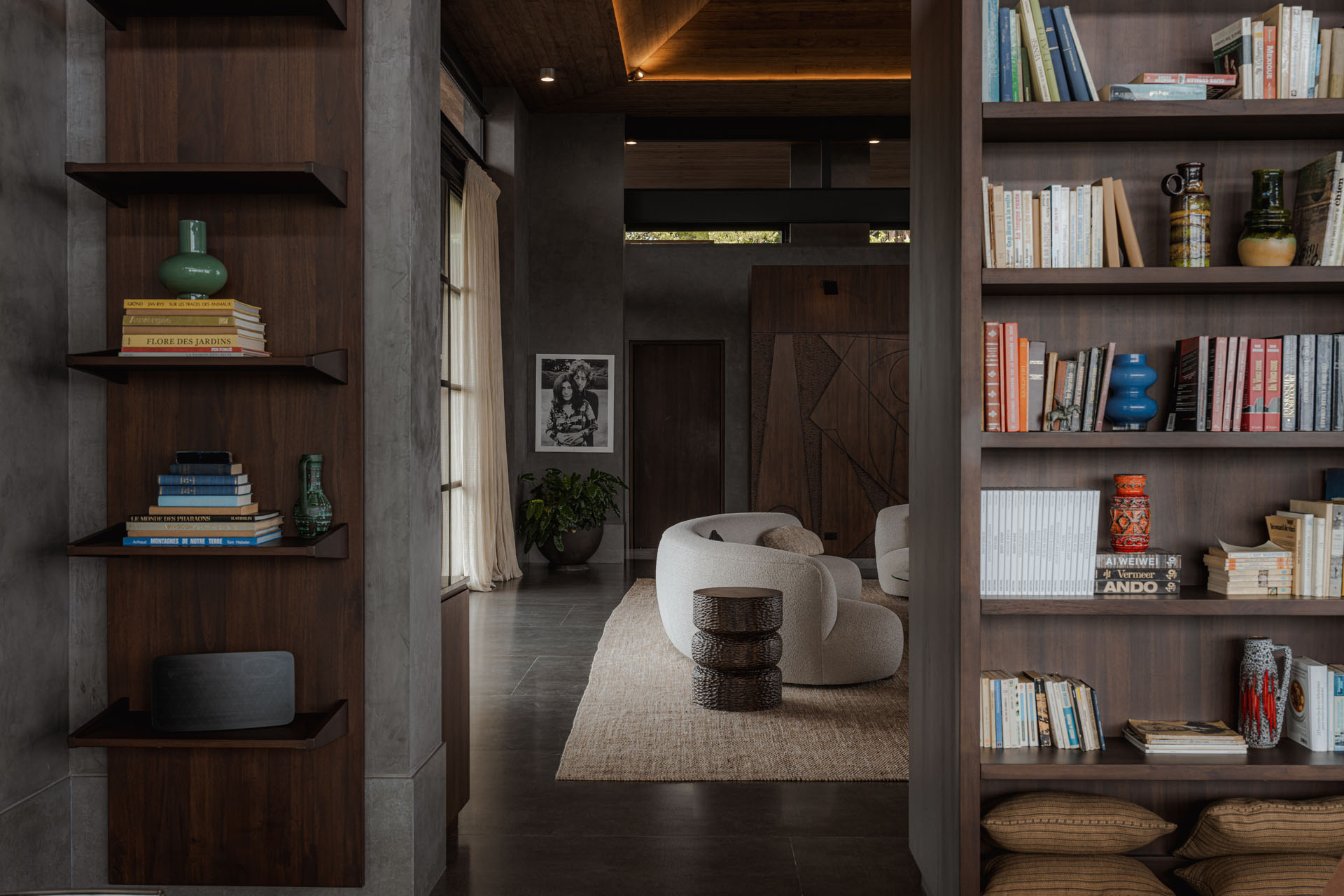 Interior architectural detail looking through custom dark wood bookshelves toward a curved seating area and carved wooden wall partition at Dos Vistas in Cabuya, Costa Rica by Studio Saxe.