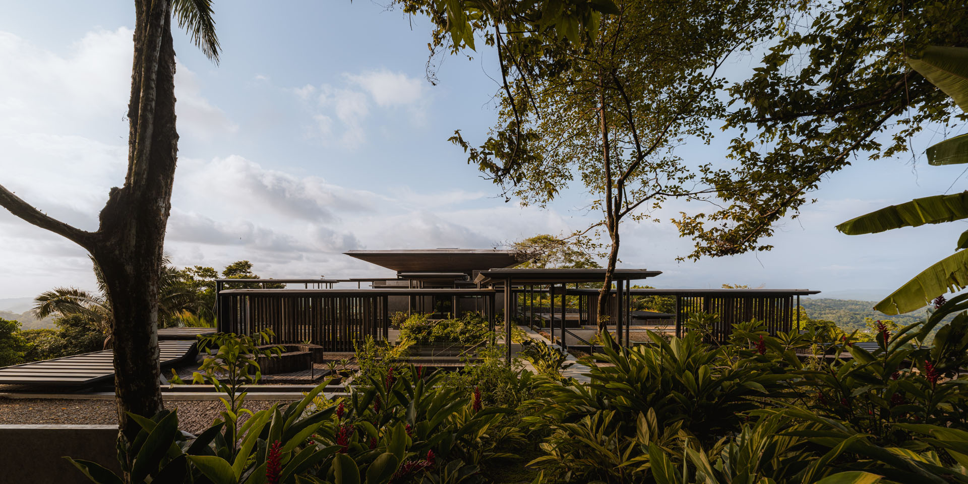 Landscape architecture view looking across terraced green roofs and vertical timber screens toward the main pavilion at Dos Vistas in Cabuya, Costa Rica by Studio Saxe.