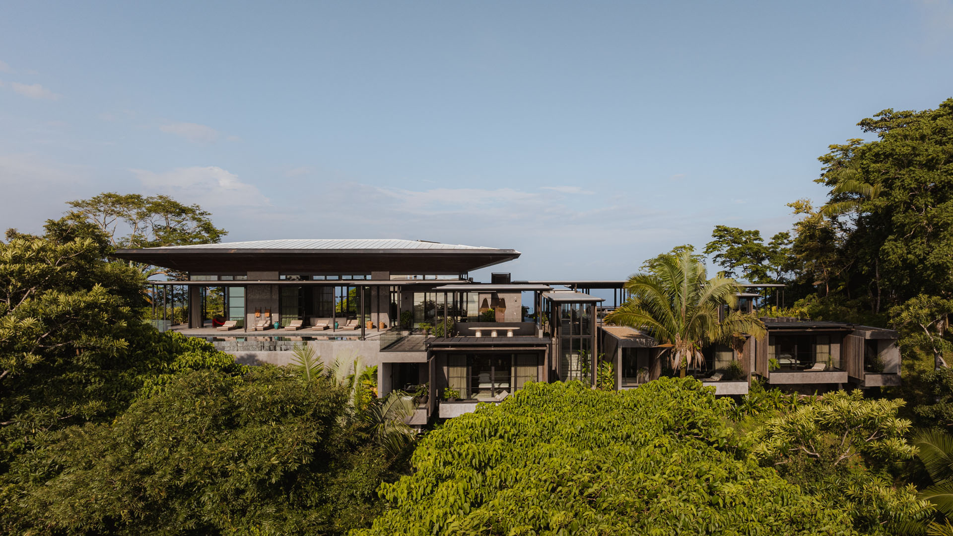 Elevated exterior view of the Dos Vistas residence showcasing the large pavilion roof, concrete volumes, and planted terraces immersed in the jungle of Cabuya, Costa Rica designed by Studio Saxe.