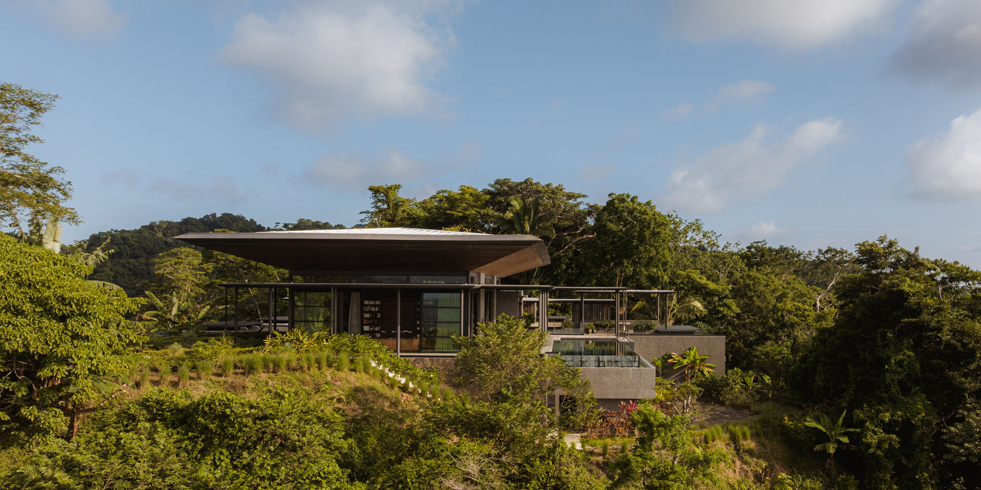 Aerial view of the Dos Vistas residence immersed in the dense jungle landscape of Cabuya, Costa Rica, showcasing the large pavilion roof and concrete terraces designed by Studio Saxe.