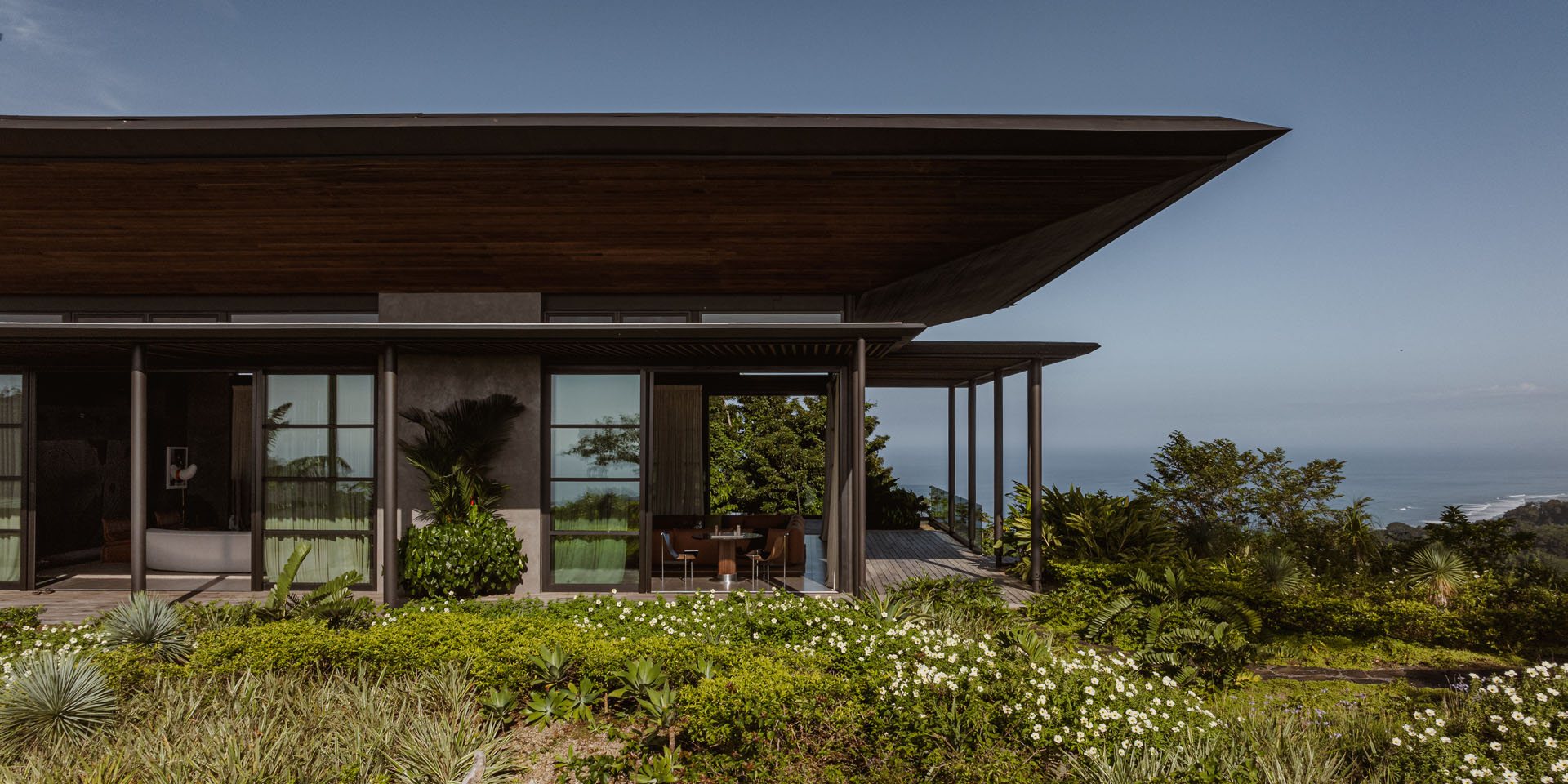 Close-up exterior detail of the deep wooden pavilion roof overhang shading the glass living spaces and outdoor terraces at Dos Vistas in Cabuya, Costa Rica by Studio Saxe.