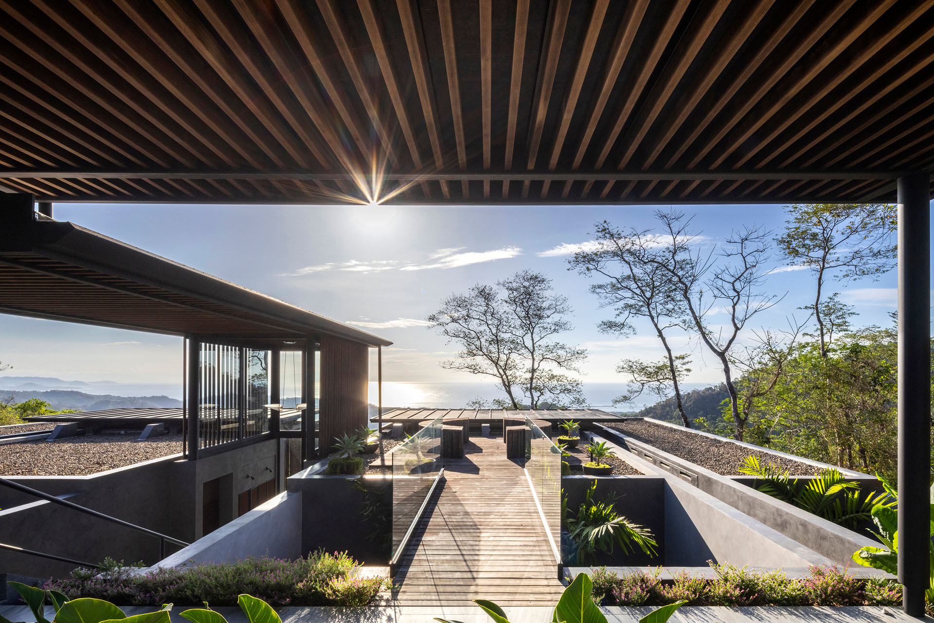 View across the landscaped rooftop terraces and wooden walkways toward the ocean horizon at the Dos Vistas residence in Cabuya, Costa Rica designed by Studio Saxe.