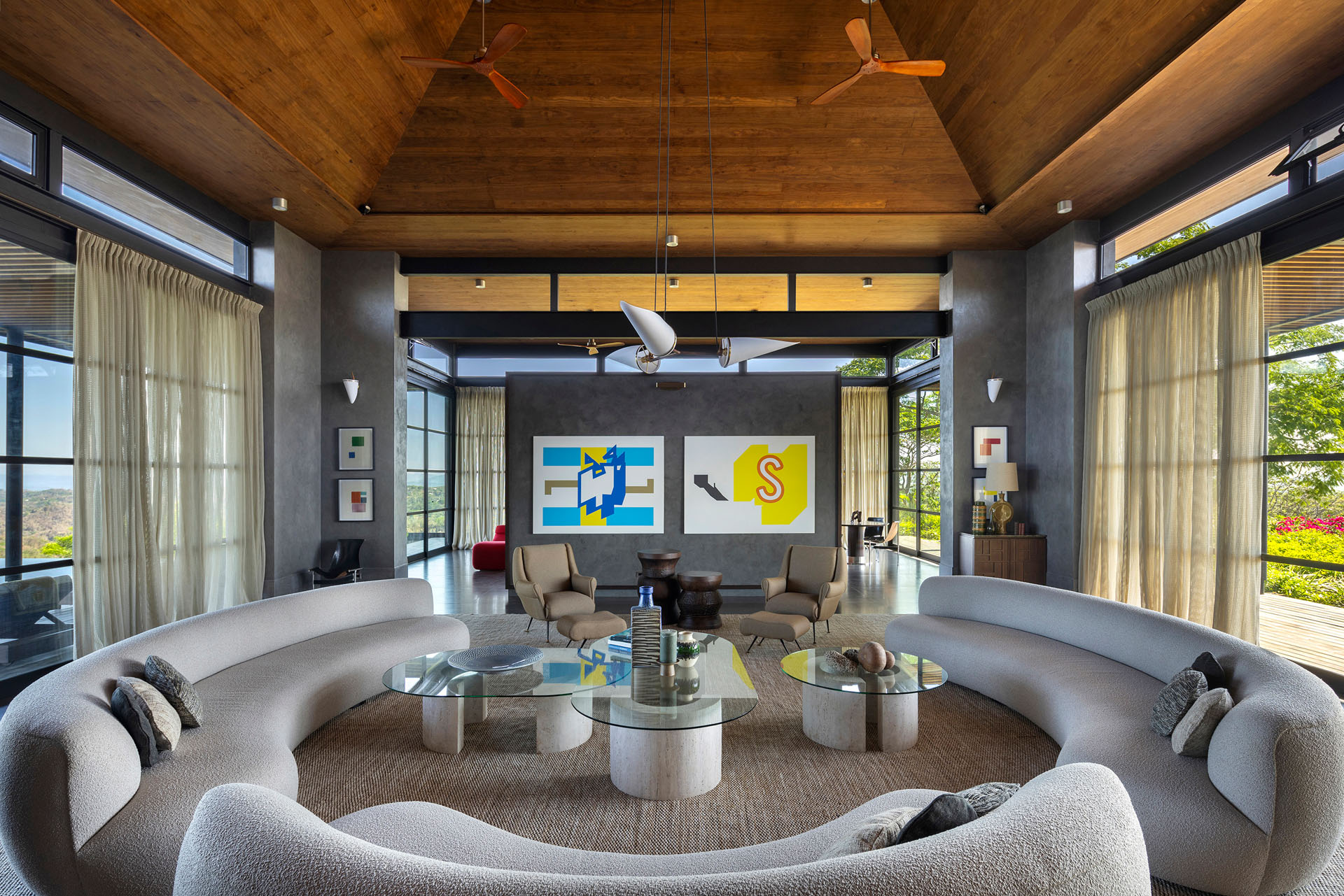 Main interior living space beneath a high vaulted timber ceiling, featuring curved sofas and cross-ventilation through large glass doors at Dos Vistas in Cabuya, Costa Rica by Studio Saxe.