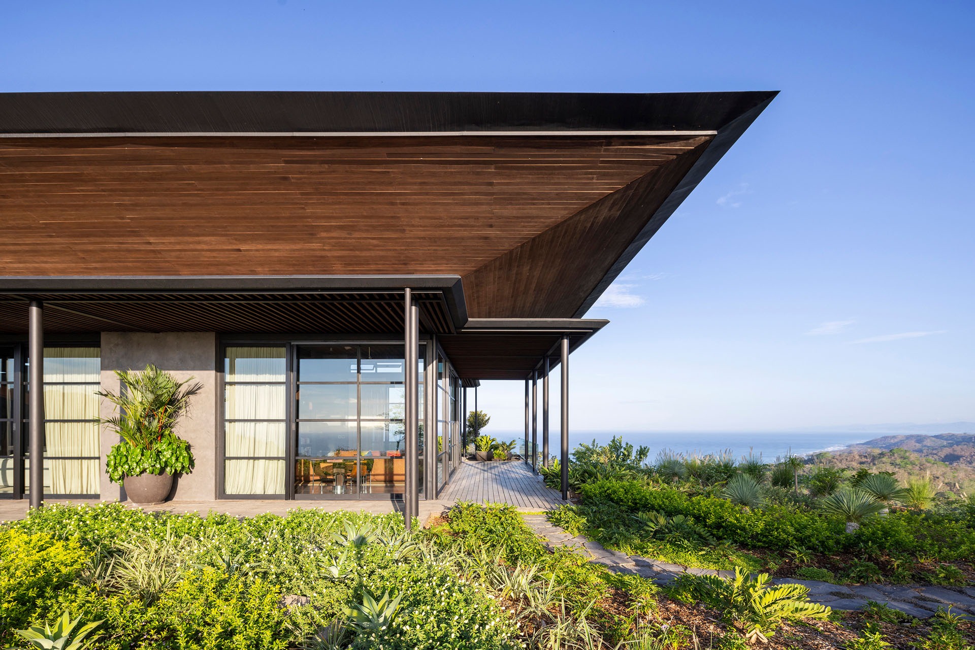 Corner exterior view of the main living pavilion highlighting the expansive timber roof overhang, glass facades, and ocean views at Dos Vistas in Cabuya, Costa Rica designed by Studio Saxe.