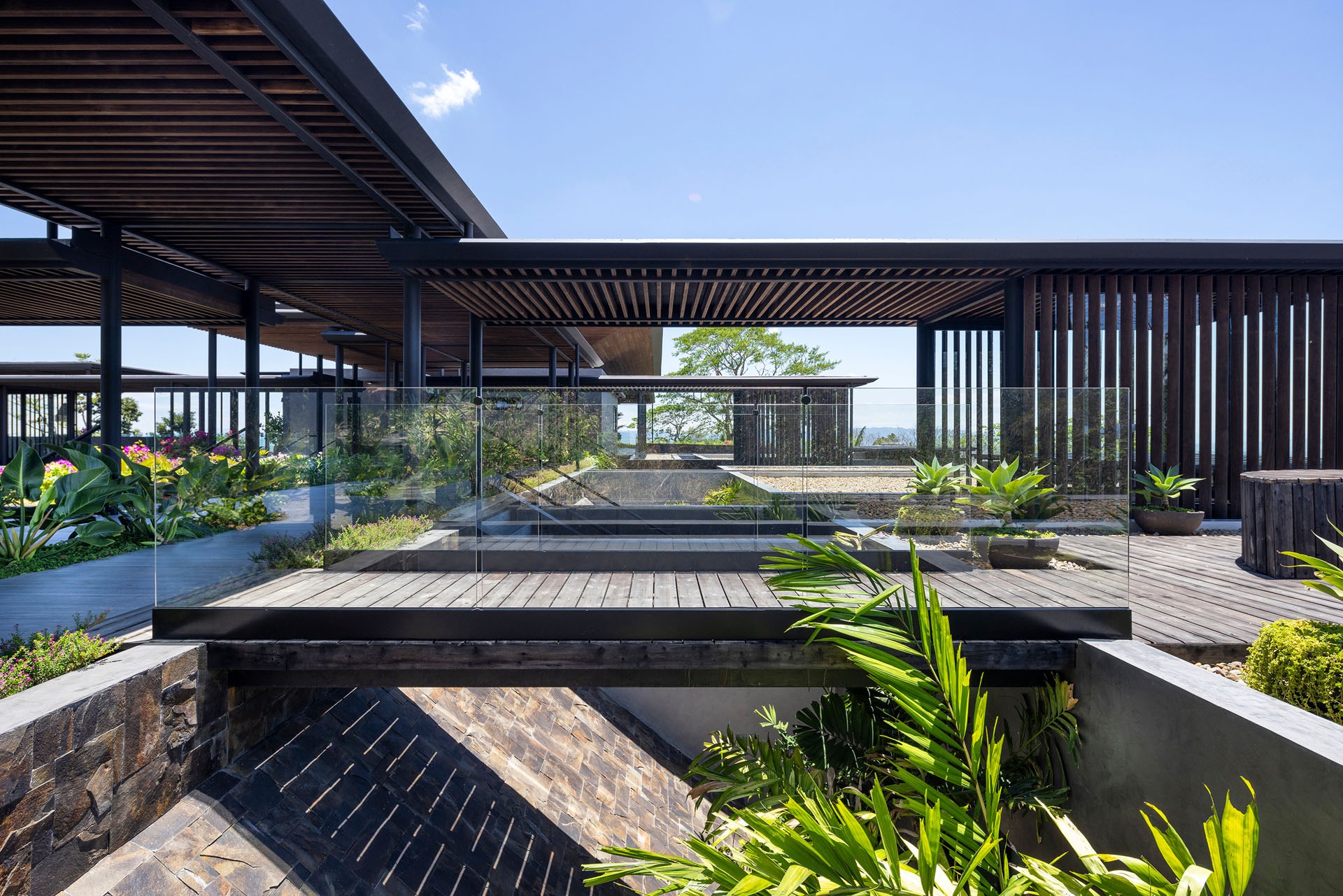 Exterior architecture showing landscaped gardens, wooden pathways, and planted terraces connecting the concrete volumes at Dos Vistas in Cabuya, Costa Rica designed by Studio Saxe.