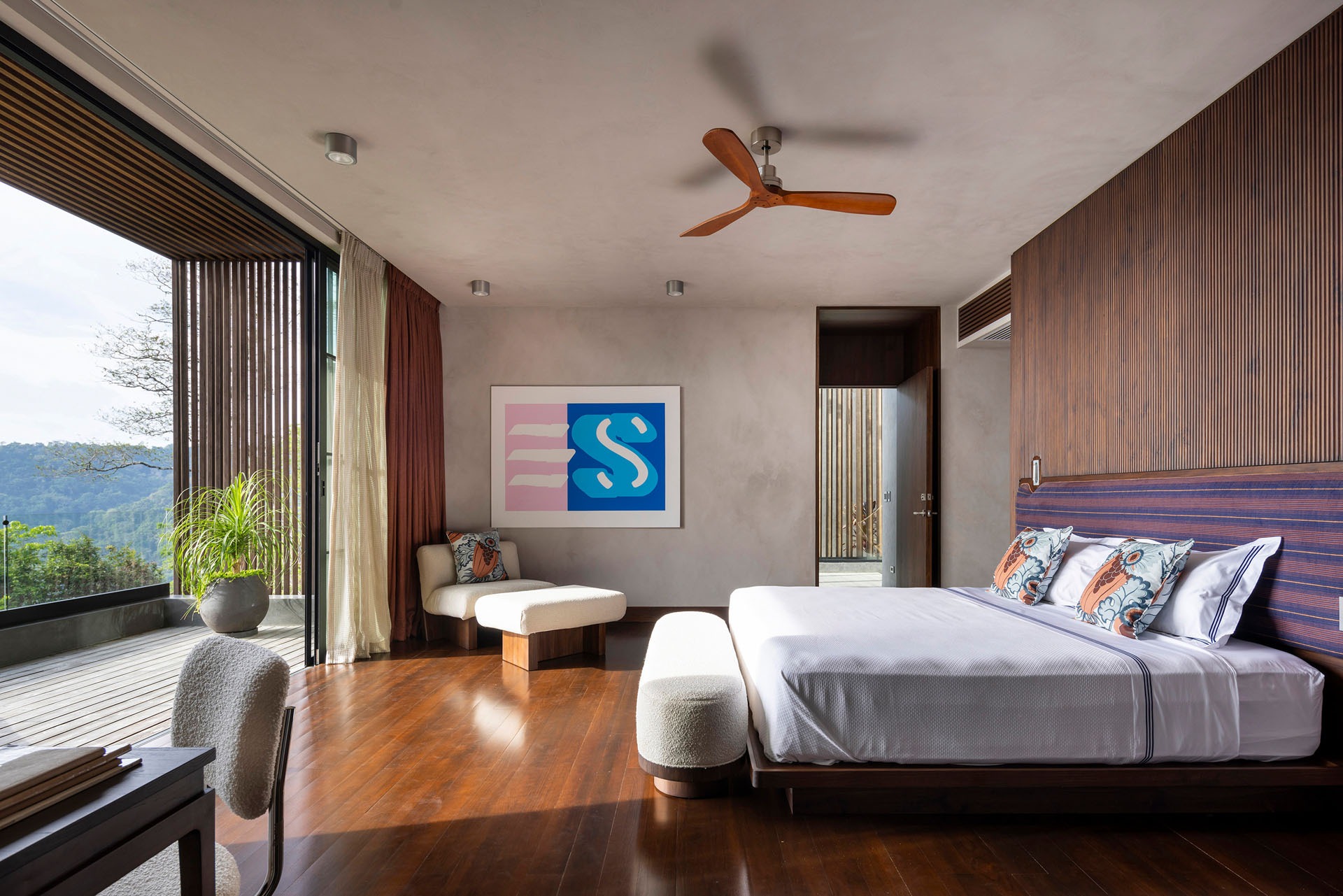 Bedroom interior featuring warm wooden floors, a timber headboard, and open sliding glass doors leading to a private balcony overlooking the jungle at Dos Vistas in Cabuya, Costa Rica by Studio Saxe.