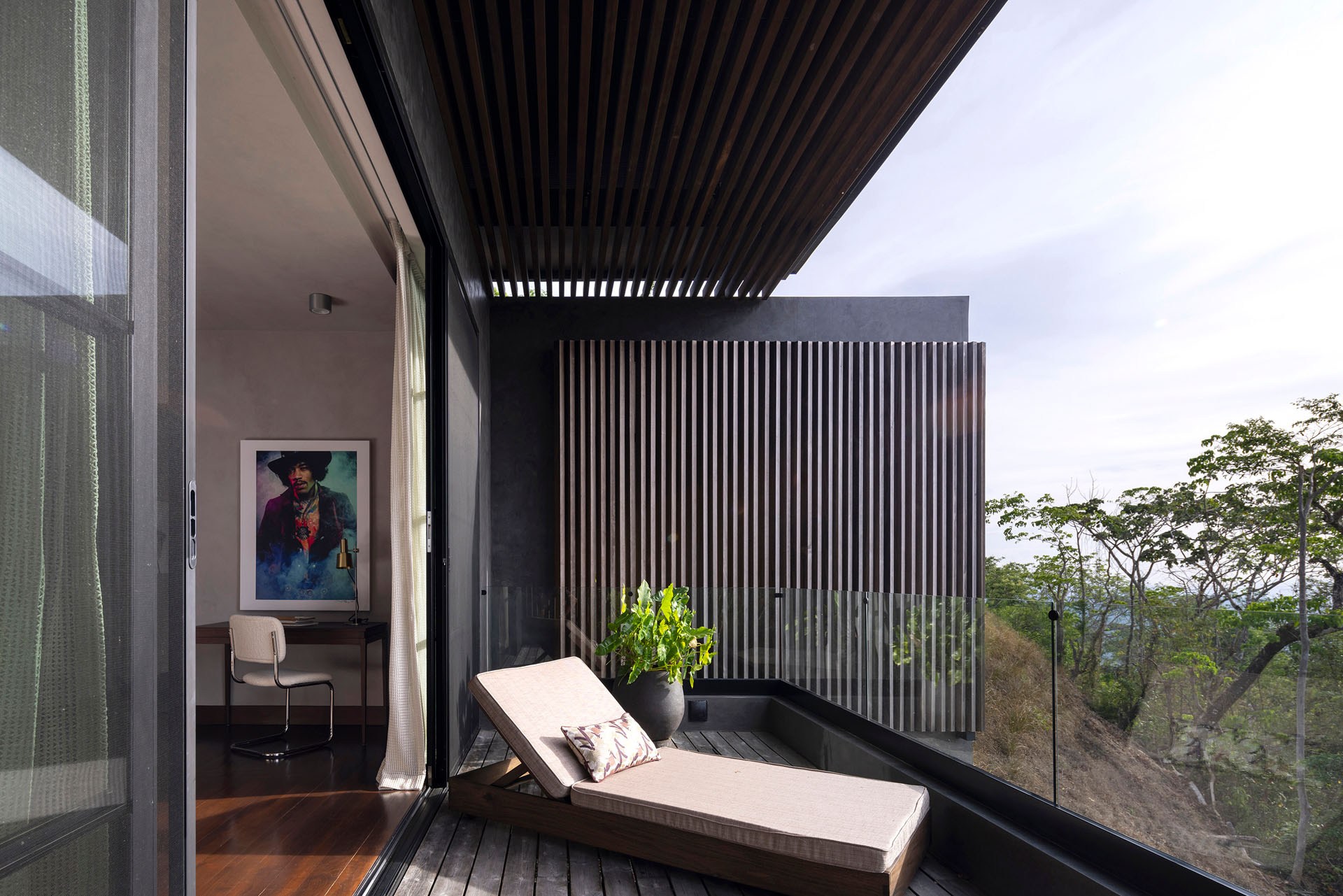 Private wooden bedroom balcony with vertical timber louvers and a lounge chair overlooking the jungle at Dos Vistas in Cabuya, Costa Rica designed by Studio Saxe.