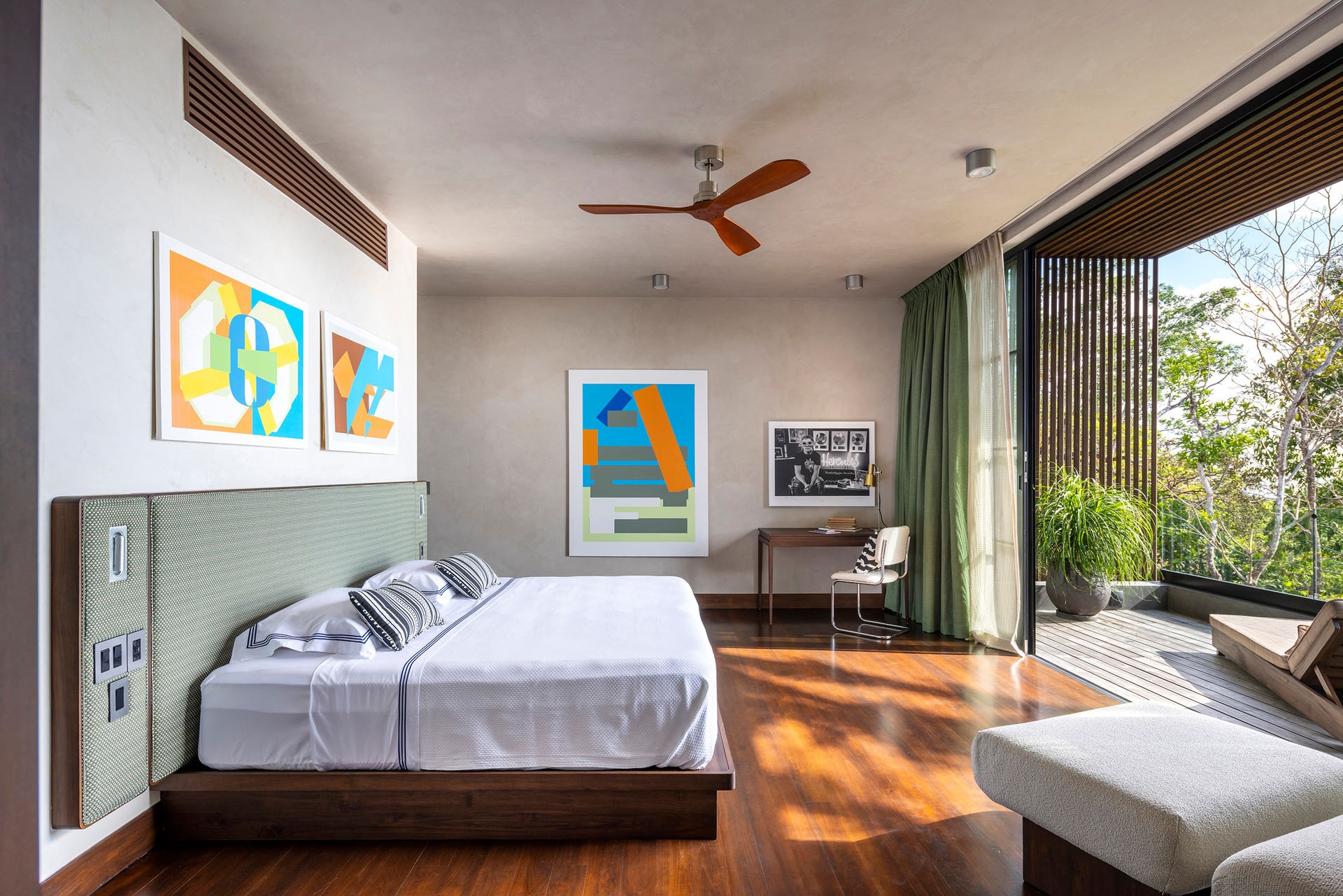 Master bedroom featuring wooden floors, green curtains, and expansive views through open balcony doors at Dos Vistas in Cabuya, Costa Rica by Studio Saxe.