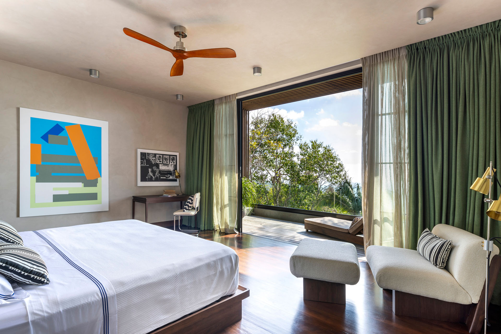Bedroom with wooden floors, modern art, and open glass doors leading to a private balcony at Dos Vistas in Cabuya, Costa Rica designed by Studio Saxe.