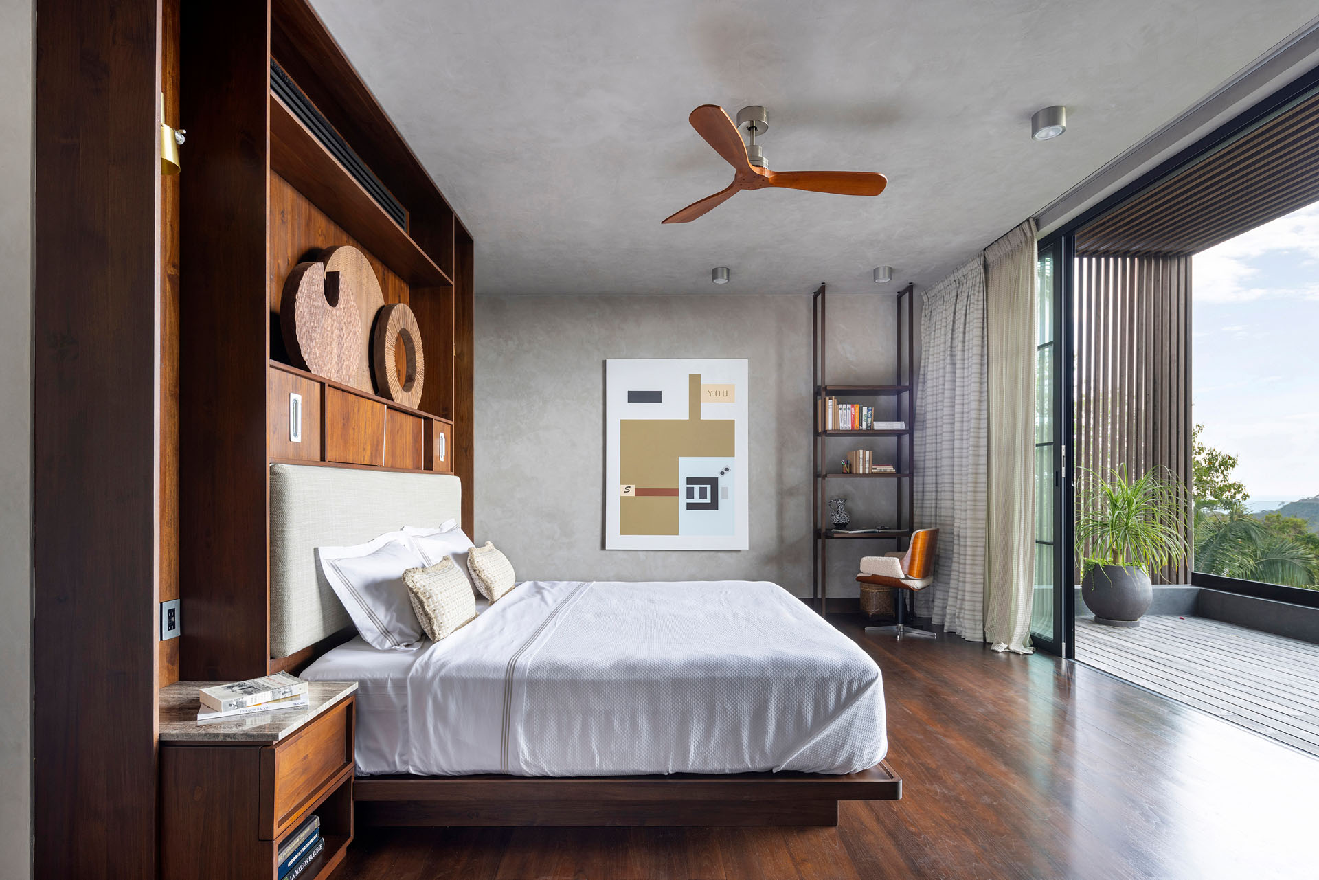Interior bedroom featuring custom built-in wooden headboard cabinetry and open glass doors to a balcony at Dos Vistas in Cabuya, Costa Rica by Studio Saxe.