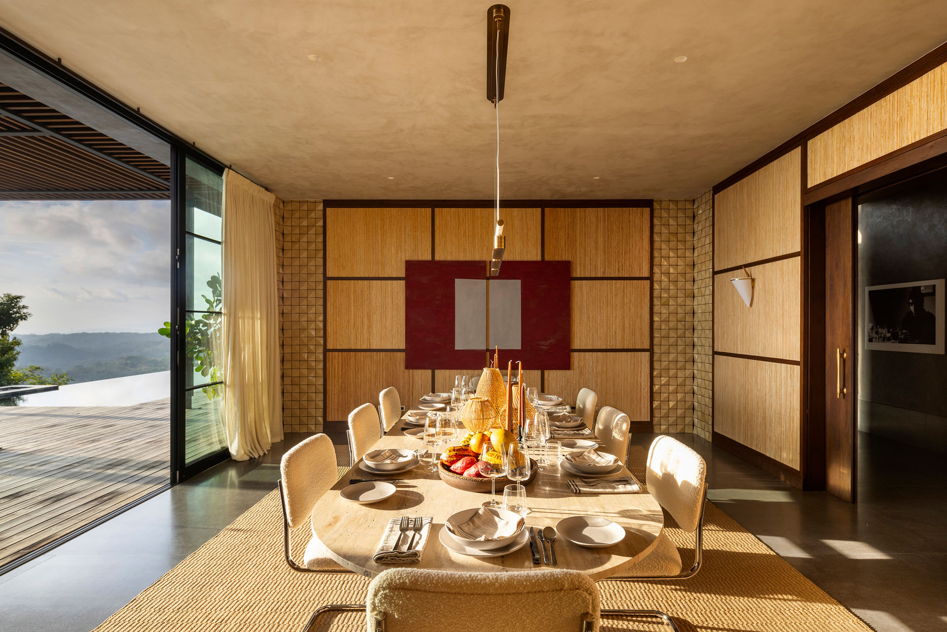 Interior dining room with woven wall details and open sliding glass doors leading to the pool terrace at Dos Vistas in Cabuya, Costa Rica by Studio Saxe.