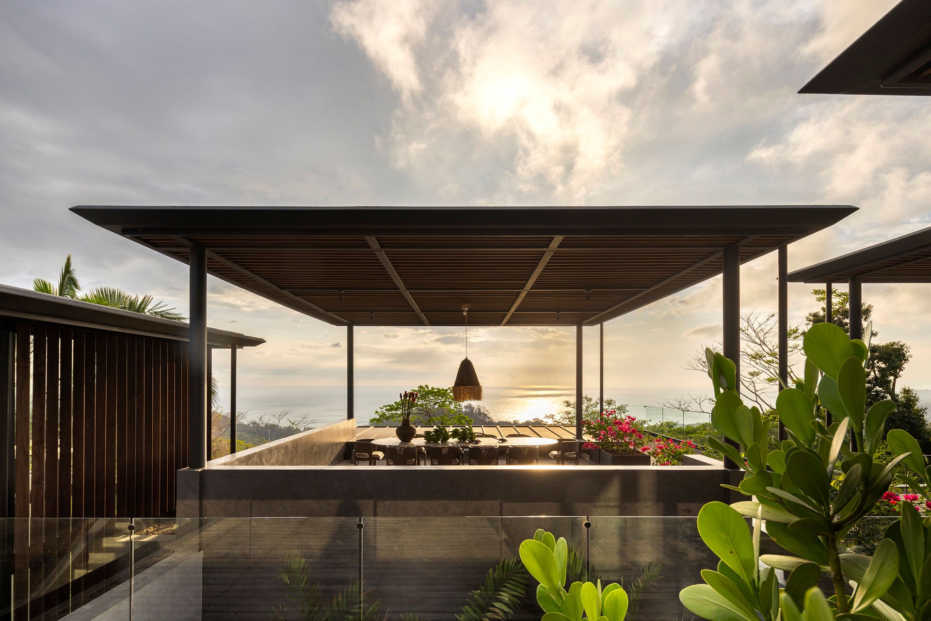 Outdoor dining terrace beneath a lightweight pavilion framing sunset ocean views at Dos Vistas in Cabuya, Costa Rica designed by Studio Saxe.